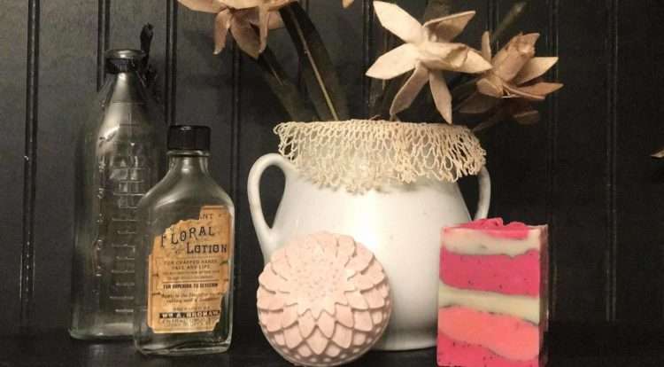 decorative fabric flowers in white pitcher, a bath bomb, a soap bar, and bottles